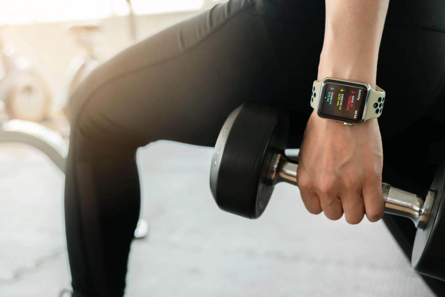 Close-up of a smartwatch showing activity rings on a wrist mid-workout, gripping a dumbbell.